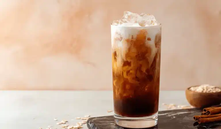 Brown sugar shaken espresso with oat milk swirl, cinnamon sticks, and oats on a marble surface