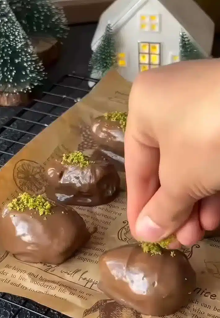 Dipping stuffed dates in chocolate and topping with crushed pistachios