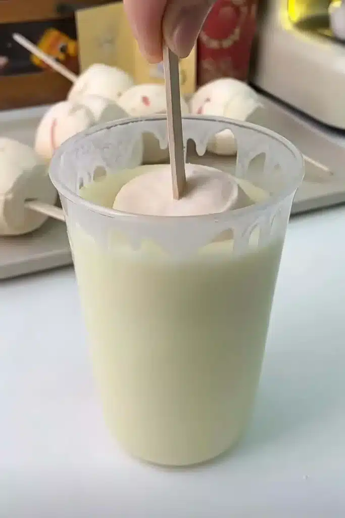 Dipping peach ice cream bar into white chocolate coating