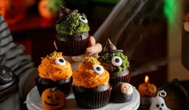 Halloween Dubai chocolate cupcakes with green pistachio and orange frosting, decorated with candy eyes and witch hats