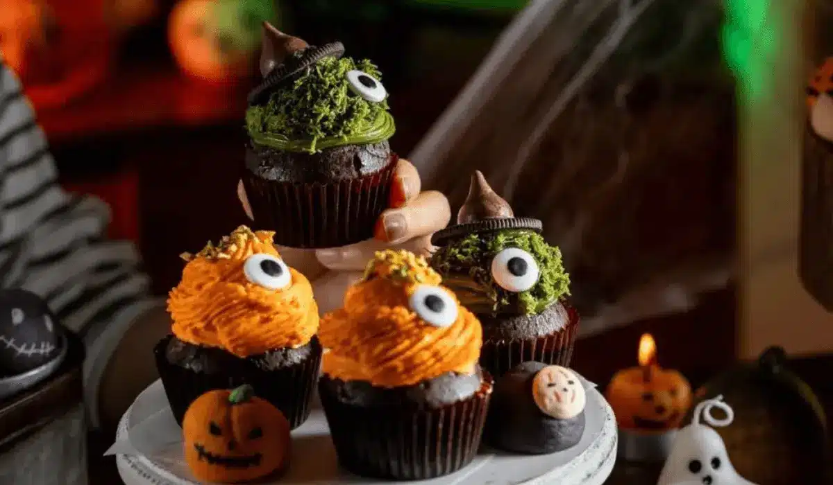 Halloween Dubai chocolate cupcakes with green pistachio and orange frosting, decorated with candy eyes and witch hats
