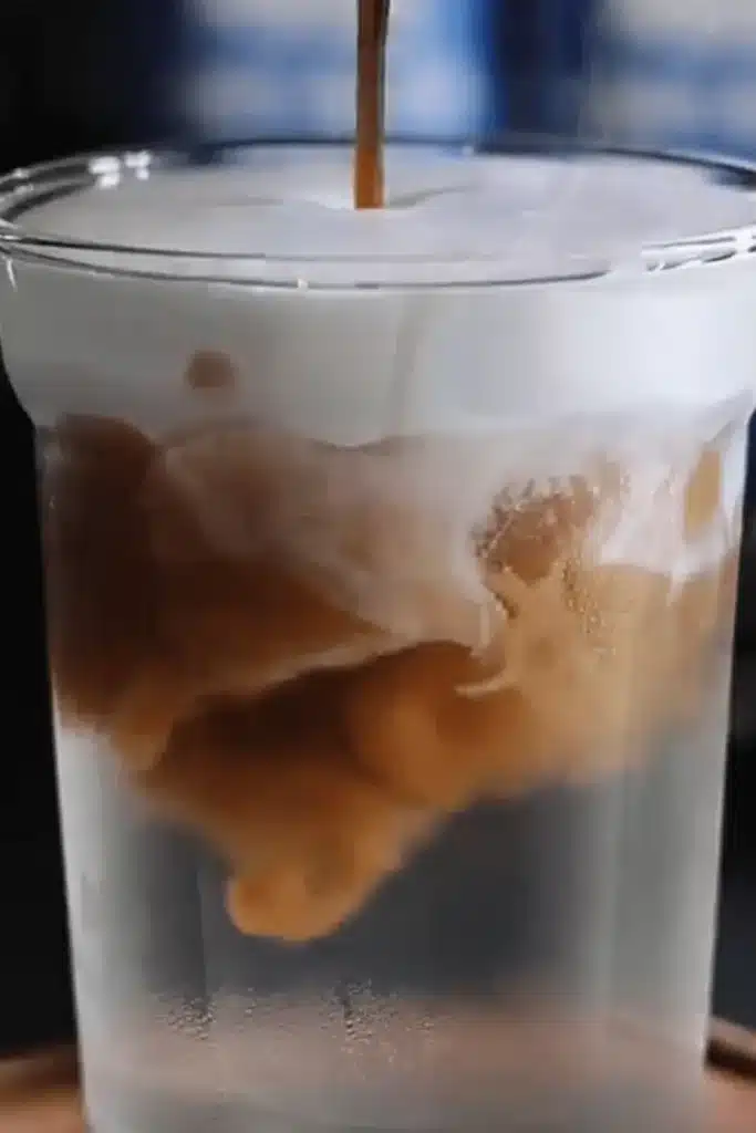 Espresso shot swirling through coconut water under cloud cream layer in Coconut Cloud Coffee