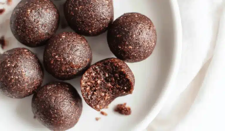 Overhead view of date brownie balls on a white plate, one with a bite