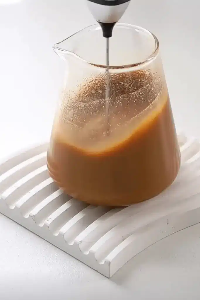 Frothing a peanut butter latte blend in a glass pitcher for smooth texture