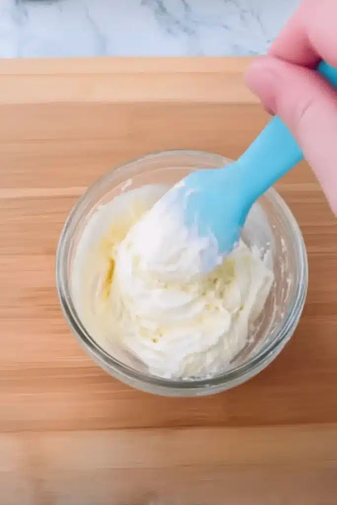 Whipping marshmallow frosting in a small glass bowl with a blue spatula
