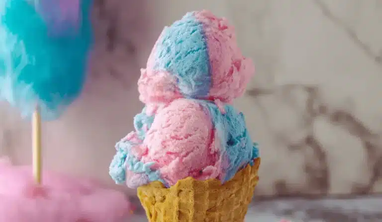 Double scoop cotton candy ice cream in a waffle cone with soft pink and blue swirls, set on a marble backdrop