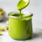 Jar of smooth bright green pistachio butter with a spoonful dripping over the top