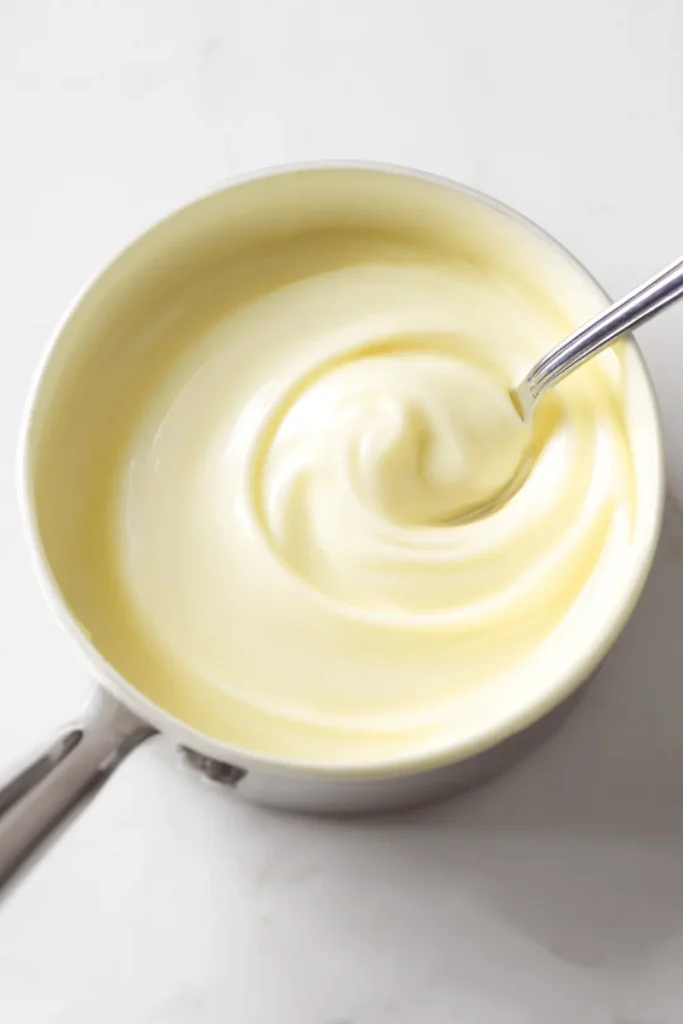 Melted white chocolate in a saucepan being stirred until smooth