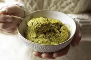 A person holding a rustic bowl of homemade Dubai chocolate filling, with a spoon showing the crunchy kataifi and pistachio texture.